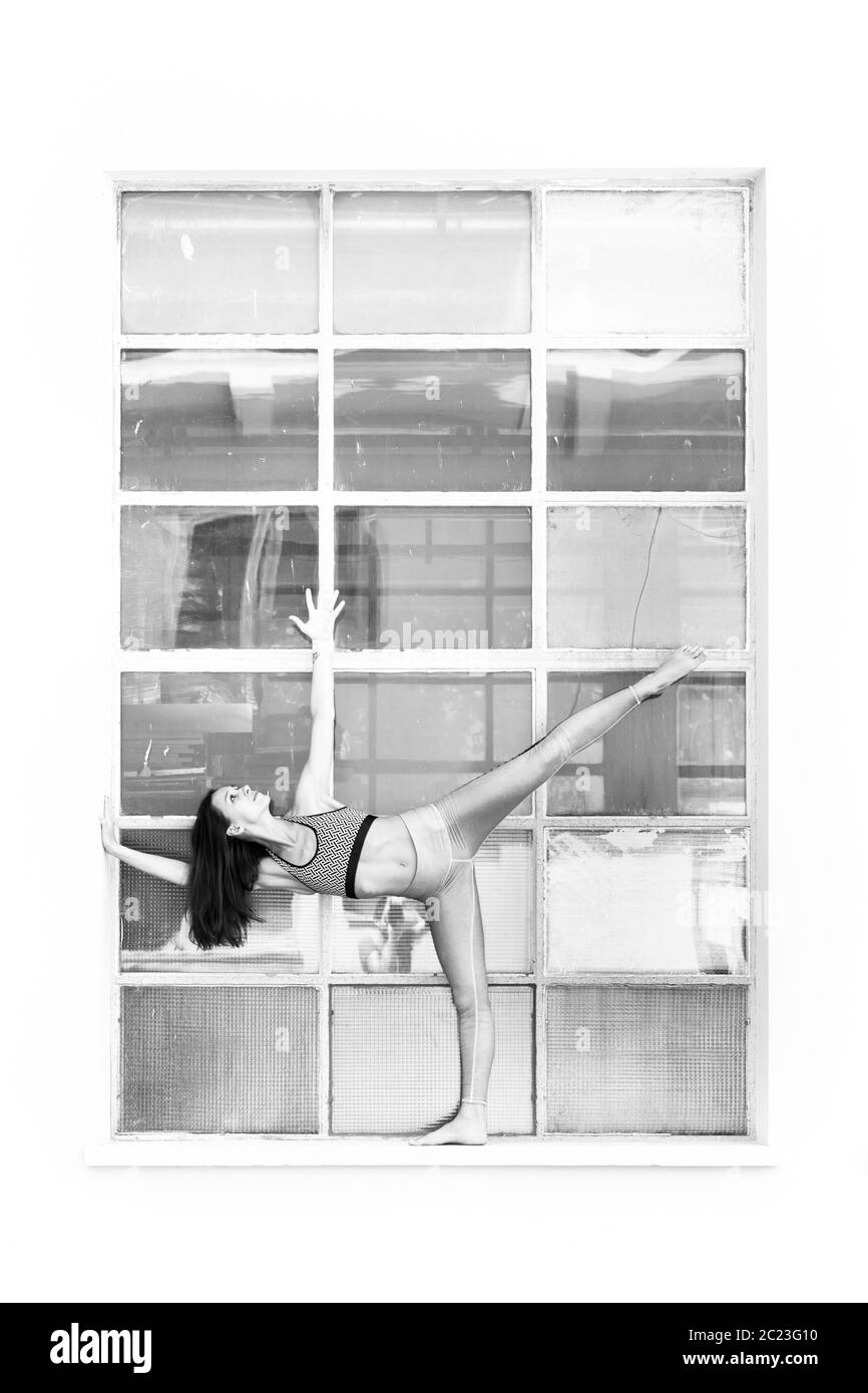 Colocar deportivo chica activa en la moda sportswear haciendo ejercicio de la aptitud del yoga en la parte delantera del bastidor de la ventana. industriales grandes coloridos reflejos en el vidrio de la ventana Foto de stock