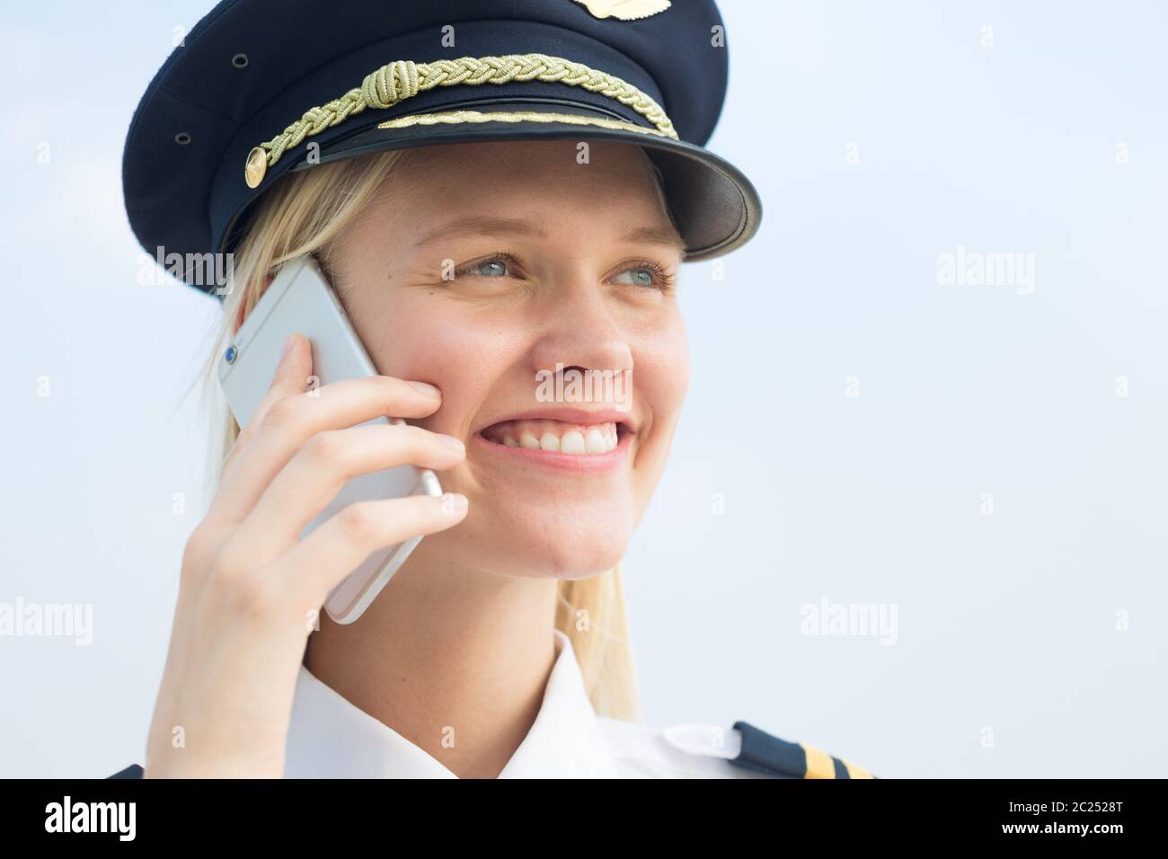 Una rubia bastante piloto mujer hablando por teléfono en el trabajo en el aeropuerto de fuera. Fondo azul de piel. Foto de stock