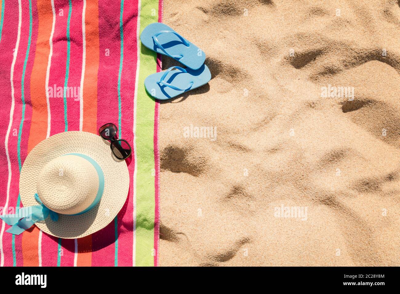 Toalla de playa multicolor con accesorios de playa en arena amarilla Foto de stock