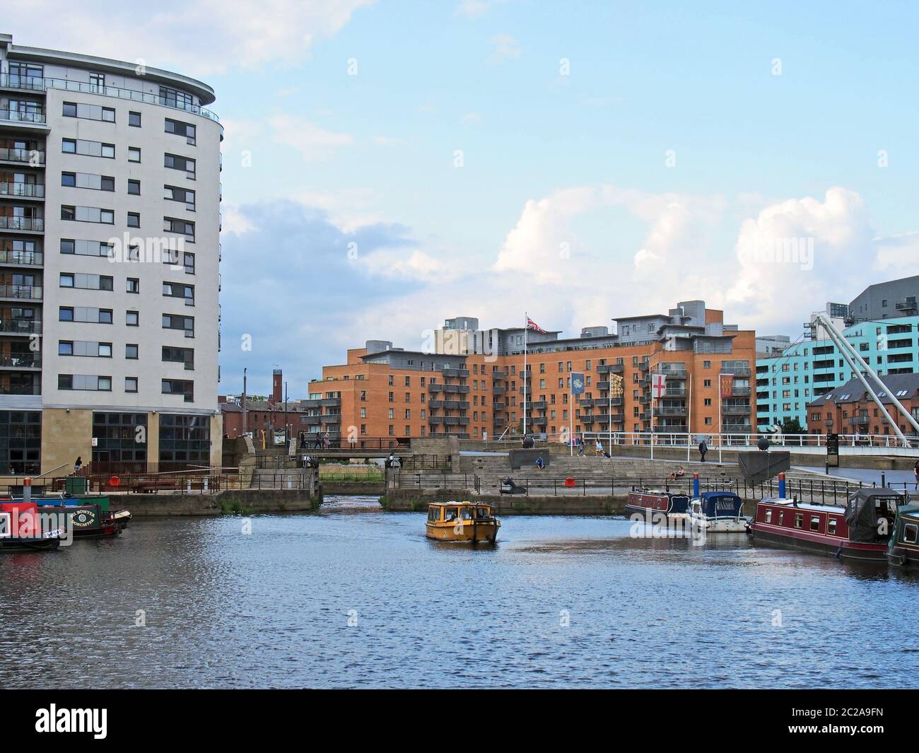 una vista de las puertas de la cerradura en el muelle de leeds con un taxi de agua amarillo y casas flotantes amarradas a lo largo del muelle Foto de stock