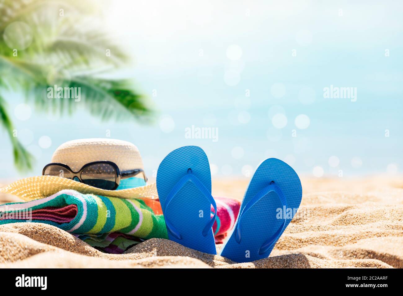 Accesorios de playa sombrero de paja, chanclas, toalla en la soleada playa tropical, vacaciones de verano Foto de stock