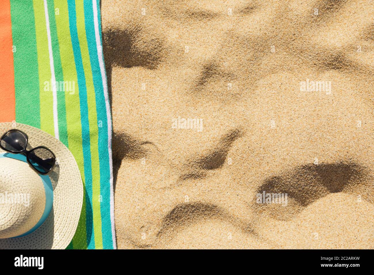 Toalla de playa con sombrero, gafas de sol y chanclas en la arena Foto de stock