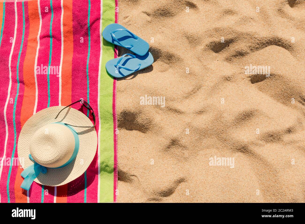 Toalla de playa con sombrero, gafas de sol y chanclas en la arena Foto de stock