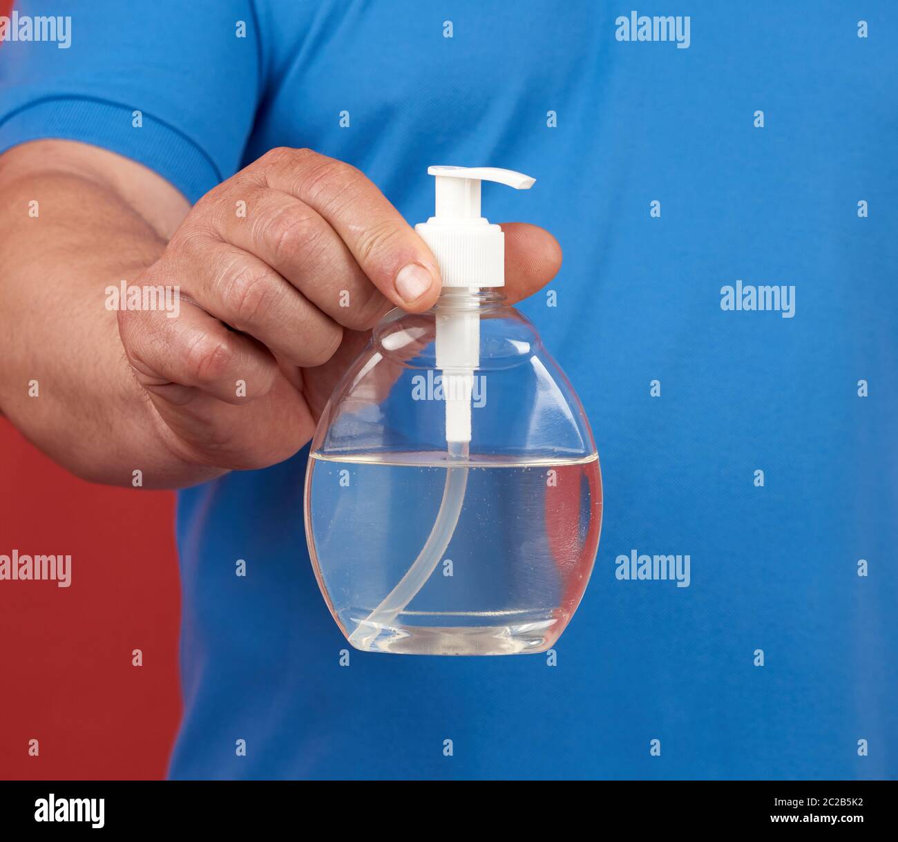 El hombre en una camiseta azul sostiene un recipiente de plástico transparente con un desinfectante de manos, un producto de higiene contra enfermedades virales Foto de stock