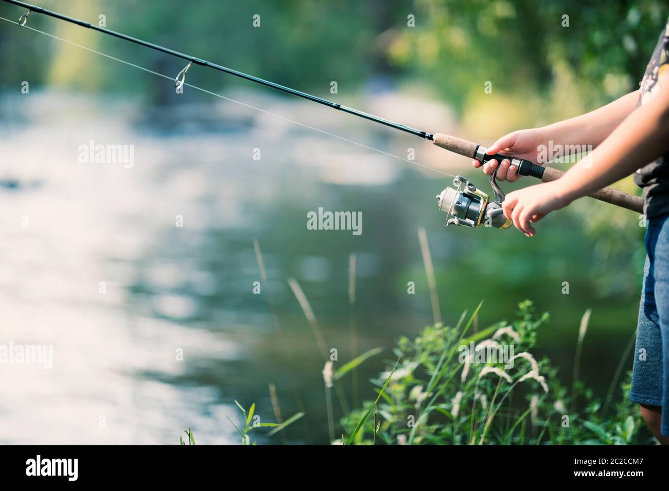 Caña de pescar y carrete en manos en el río Foto de stock