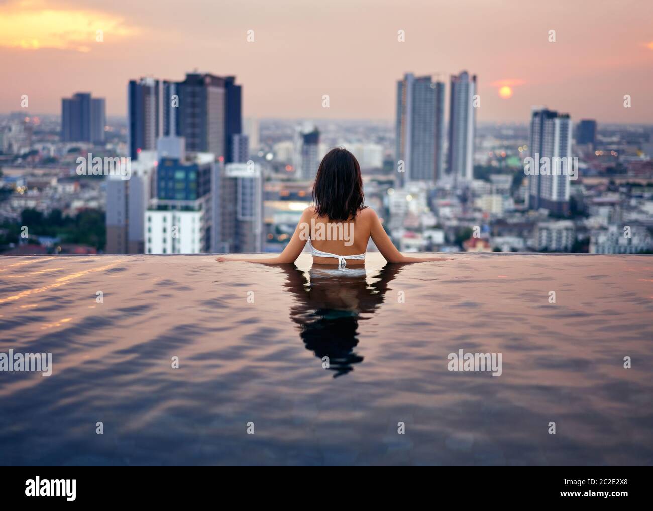 Mujer joven relajarse en la piscina en la azotea durante la puesta de sol increíble y disfrutar de la vista de la ciudad Foto de stock