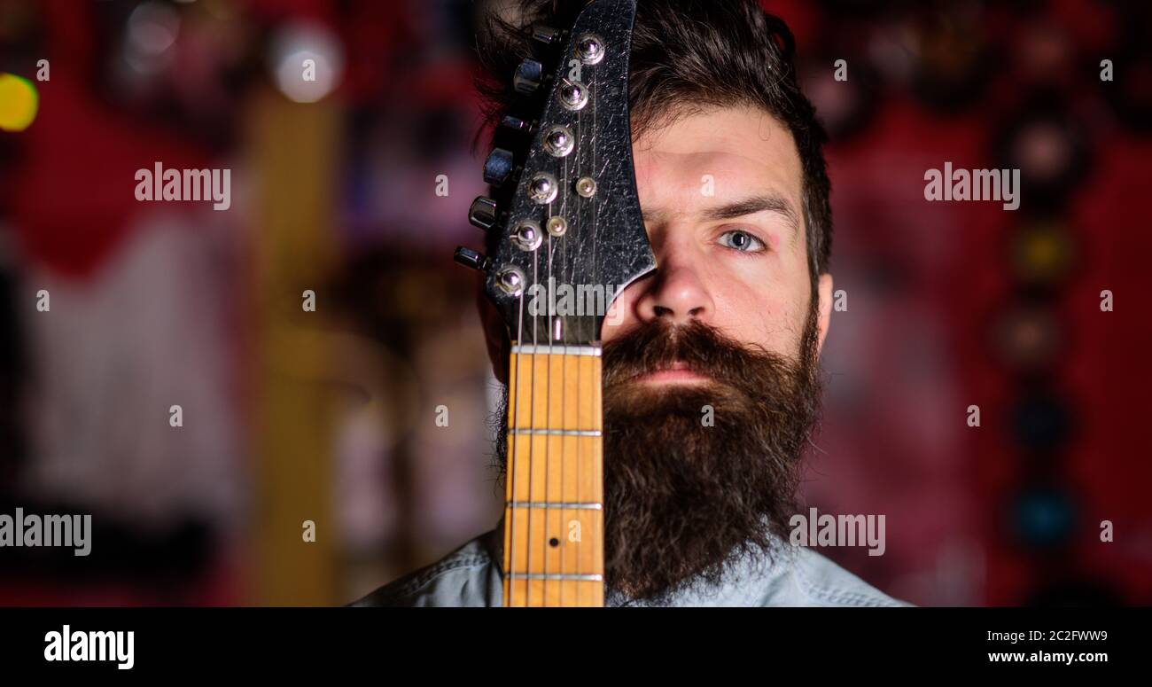 Músico, artista en cara penista, tranquila y cuello de guitarra. Hombre con  barba y bigote cubre la mitad de la cara con cuello de guitarra, de cerca.  Hombre en la sala de