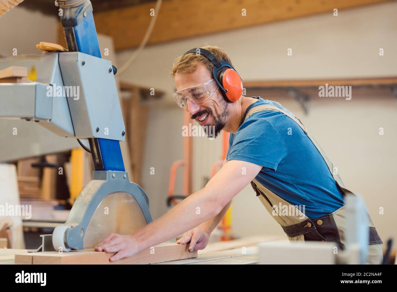 Carpintero diligente con diversión en el trabajo aserrando un pedazo de madera Foto de stock