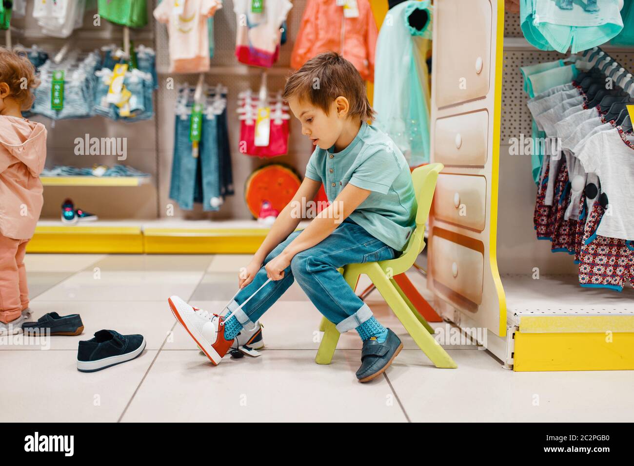 Niño pequeño intentando zapatos en la tienda de los niños, vista lateral.  Hijo escogiendo zapatillas en supermercado, compras familiares, cliente  joven Fotografía de stock - Alamy