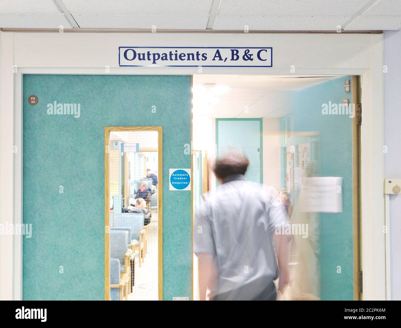 Ocupado Reino Unido NHS hospital y servicios de atención sanitaria ambulatorios en un hospital británico. Pacientes sentados, caminando y moviéndose y médico pasando por las puertas Foto de stock