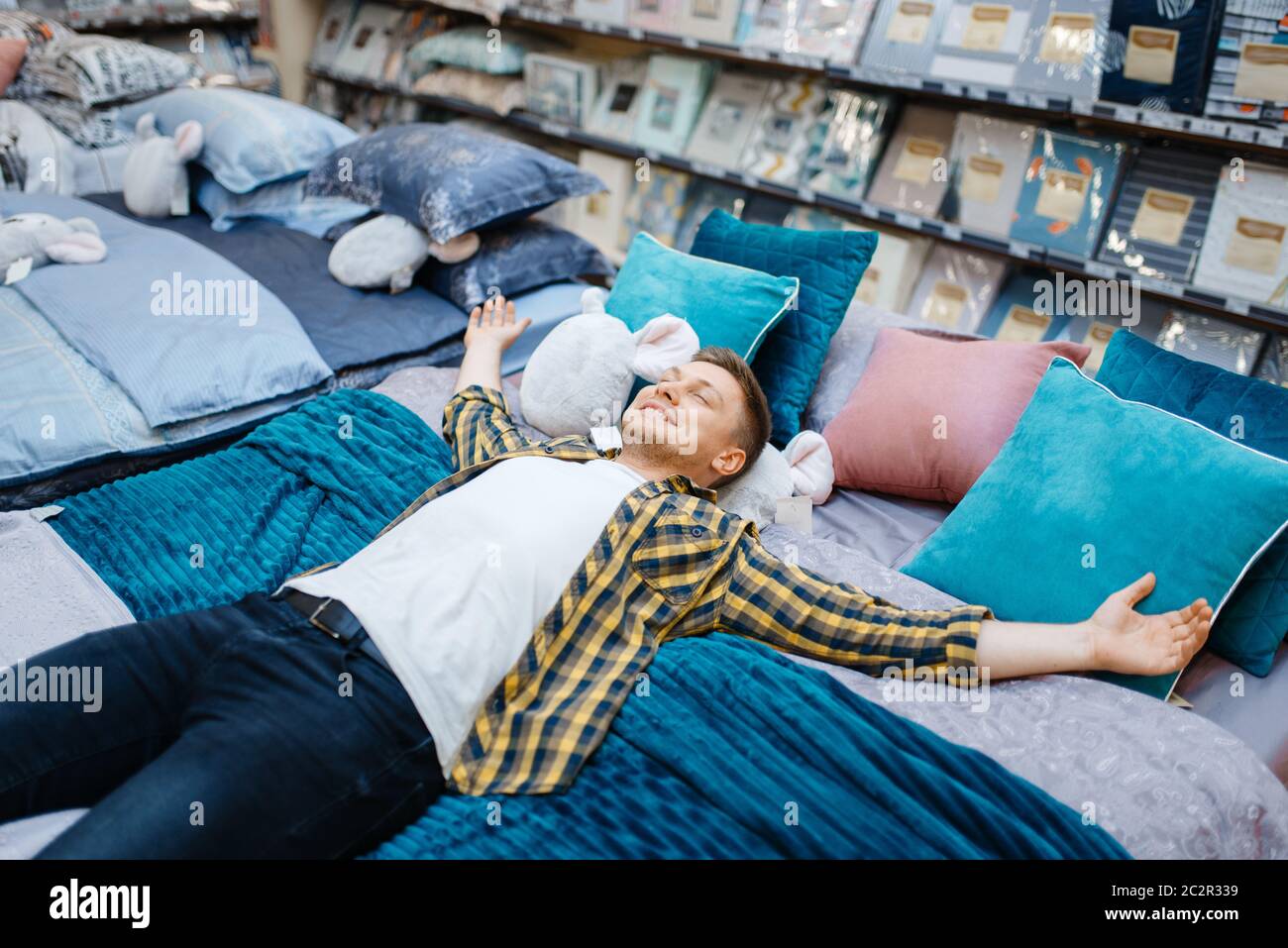 Hombre joven acostado en la cama en la tienda de ropa de Hombre persona que compra bienes de casa en el mercado, hombre que duerme en la tienda Fotografía de stock -