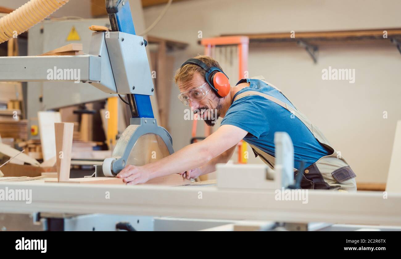 Carpintero diligente con diversión en el trabajo aserrando un pedazo de madera Foto de stock