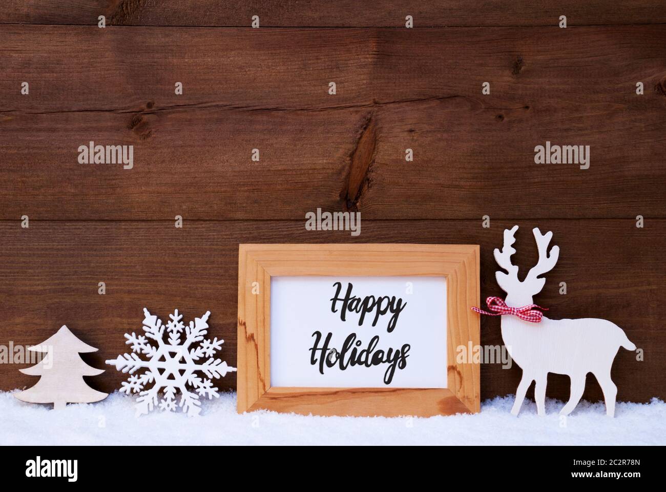 Caligrafía Egnlish Felices Fiestas. White Christmas Ornament como copo de nieve, árbol de madera y ciervo. Fondo de madera con nieve Foto de stock