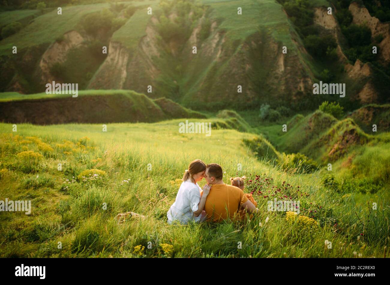 Familia con una hija pequeña descansa mientras camina en el prado sobre el fondo del barranco. Vista posterior. Foto de stock