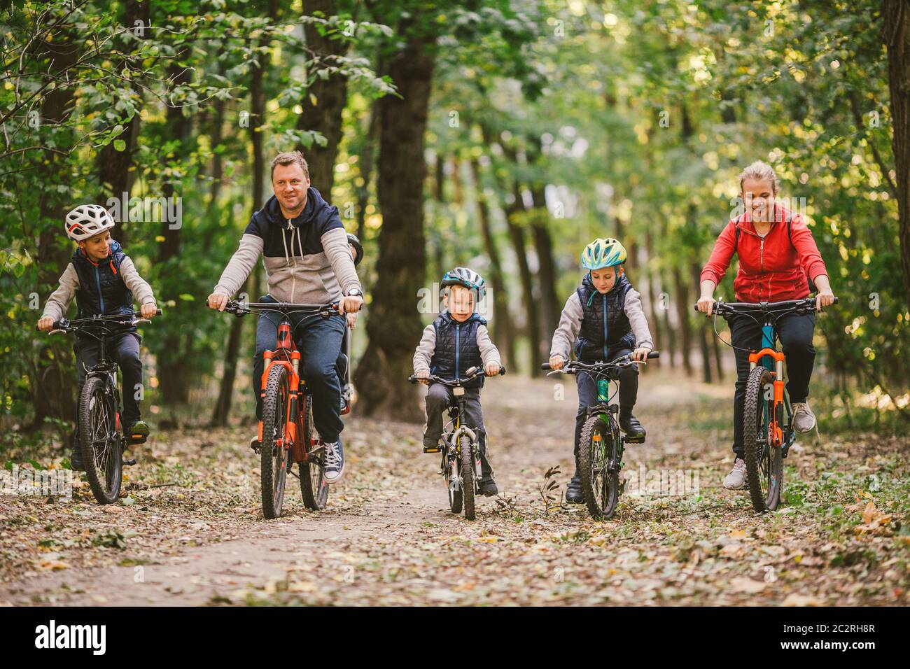 padres y niños en bicicleta en el sendero del bosque. Familia joven en  bicicleta ropa caliente en el parque de otoño. Familia bicicleta de montaña  en el bosque Fotografía de stock -