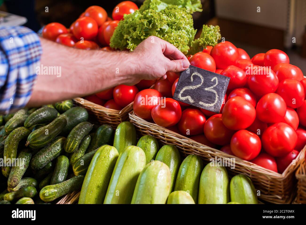 Los vendedores establecen la etiqueta de precio en los tomates rojos almacenados en una cesta de madera. Foto de stock