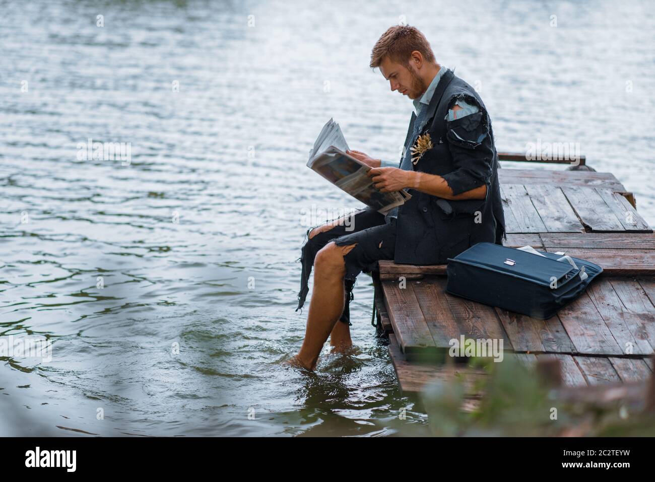 Hombre de negocios en traje rasgado leyendo el periódico en la isla del desierto. Riesgo de negocio, colapso o concepto de bancarrota Foto de stock