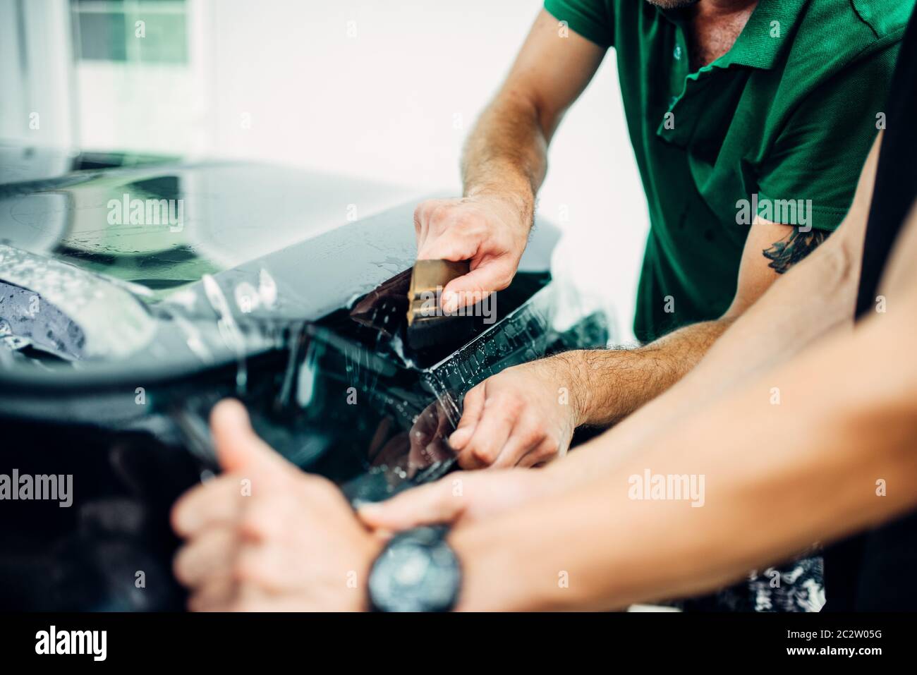 La envoltura de coches, mecánica con squeegee instala película o lámina  protectora de vinilo en la capucha del vehículo. El trabajador hace auto  detallando. Protección de la pintura del automóvil Fotografía de