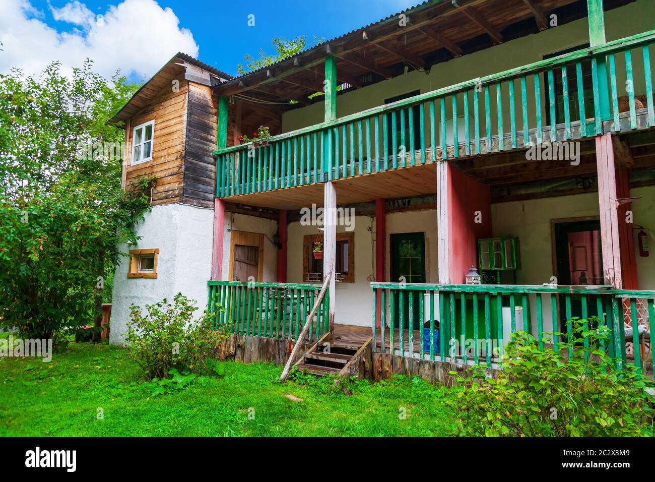 Casa de campo de dos pisos para vivir en el verano en la casa de campo de  madera con un balcón azul y una veranda, una escalera antigua, contra la  parte trasera