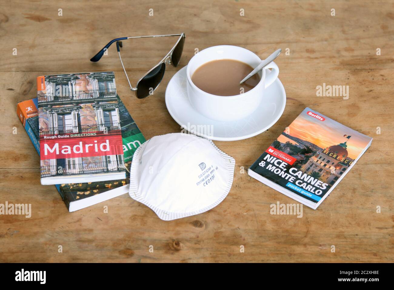 Libros de viaje con máscara y taza de té en té blanco sobre mesa de madera Foto de stock