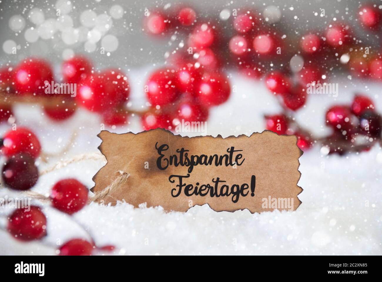 Etiqueta quemada con caligrafía alemana Entspannte Feiertage significa Feliz Navidad. Rojo Decoración de Navidad con Nieve y copos de nieve Foto de stock