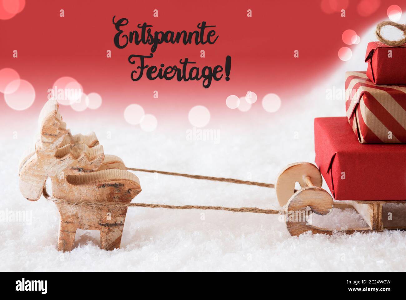 Renos y trineo con regalos de Navidad y nieve. Fondo roja brillante con caligrafía alemana Entspannte Feiertage significa ¡Feliz Navidad! Foto de stock