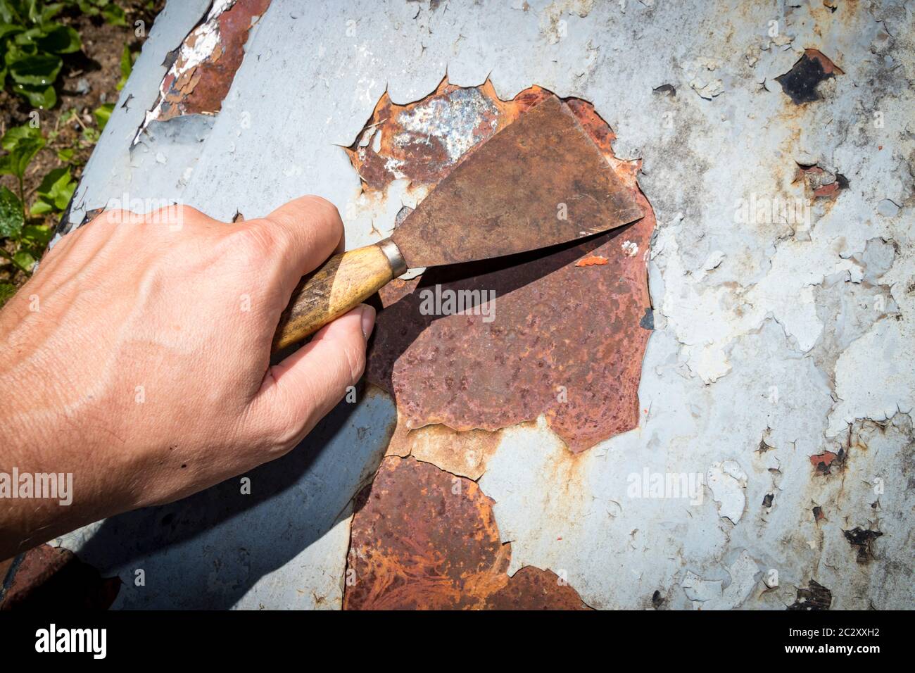 El hombre quita la pintura y el óxido de las puertas de metal usando un  rascador de pintura de metal Fotografía de stock - Alamy