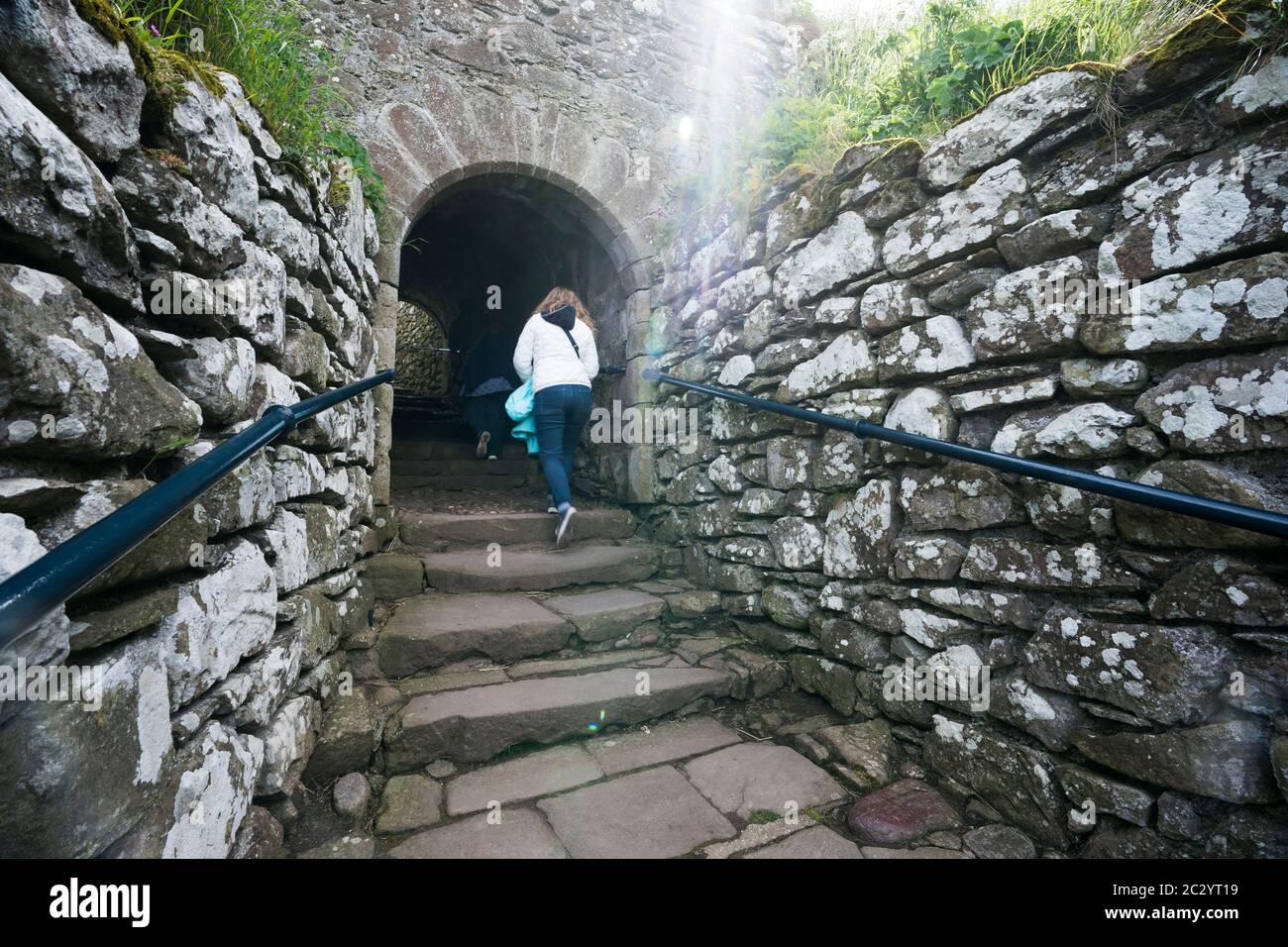 Dos personas que caminan por las escaleras de piedra en una ruina abandonada hacia el castillo de Dunnottar en Escocia, Reino Unido, Europa Foto de stock