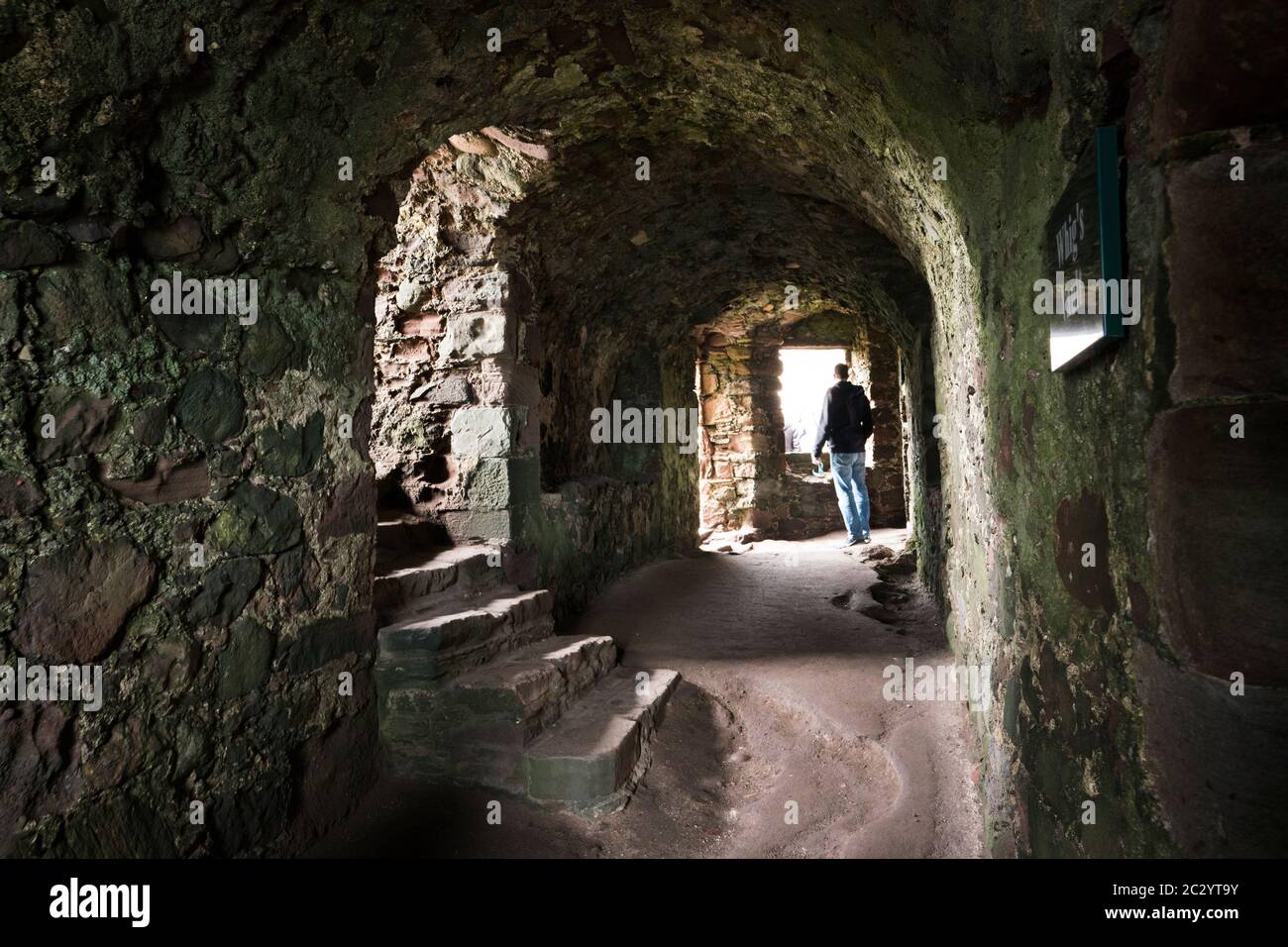 Un hombre adulto explora una antigua ruina de piedra abandonada con un techo curvado a lo largo del pasillo con escaleras y una ventana dentro del castillo de Dunnottar; Escocia, Foto de stock