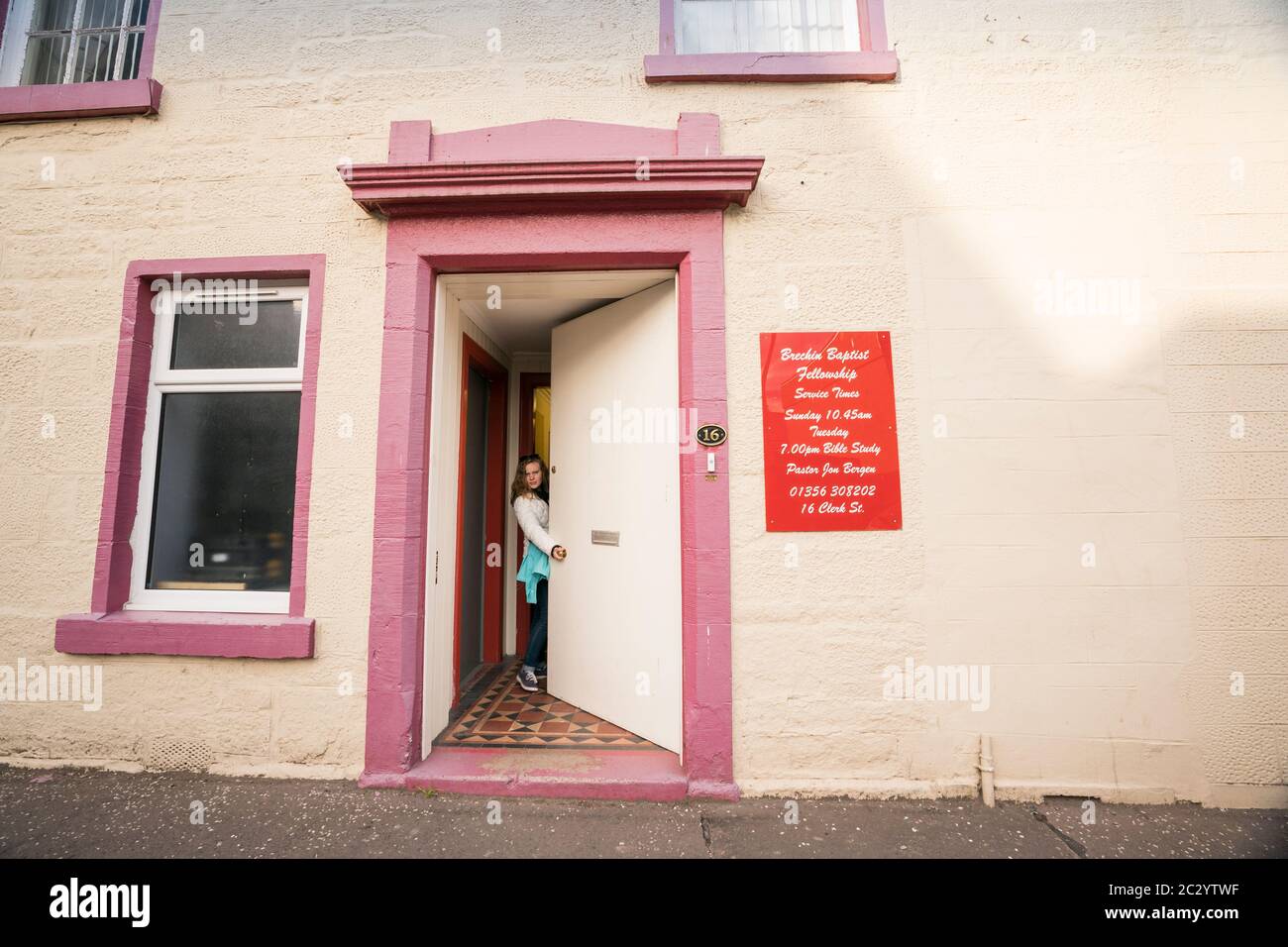 Una mujer en jeans abre la puerta a una iglesia Bautista ubicada dentro del edificio que una vez sirvió como una taberna local en la pequeña ciudad de Brechin, Escocia Foto de stock