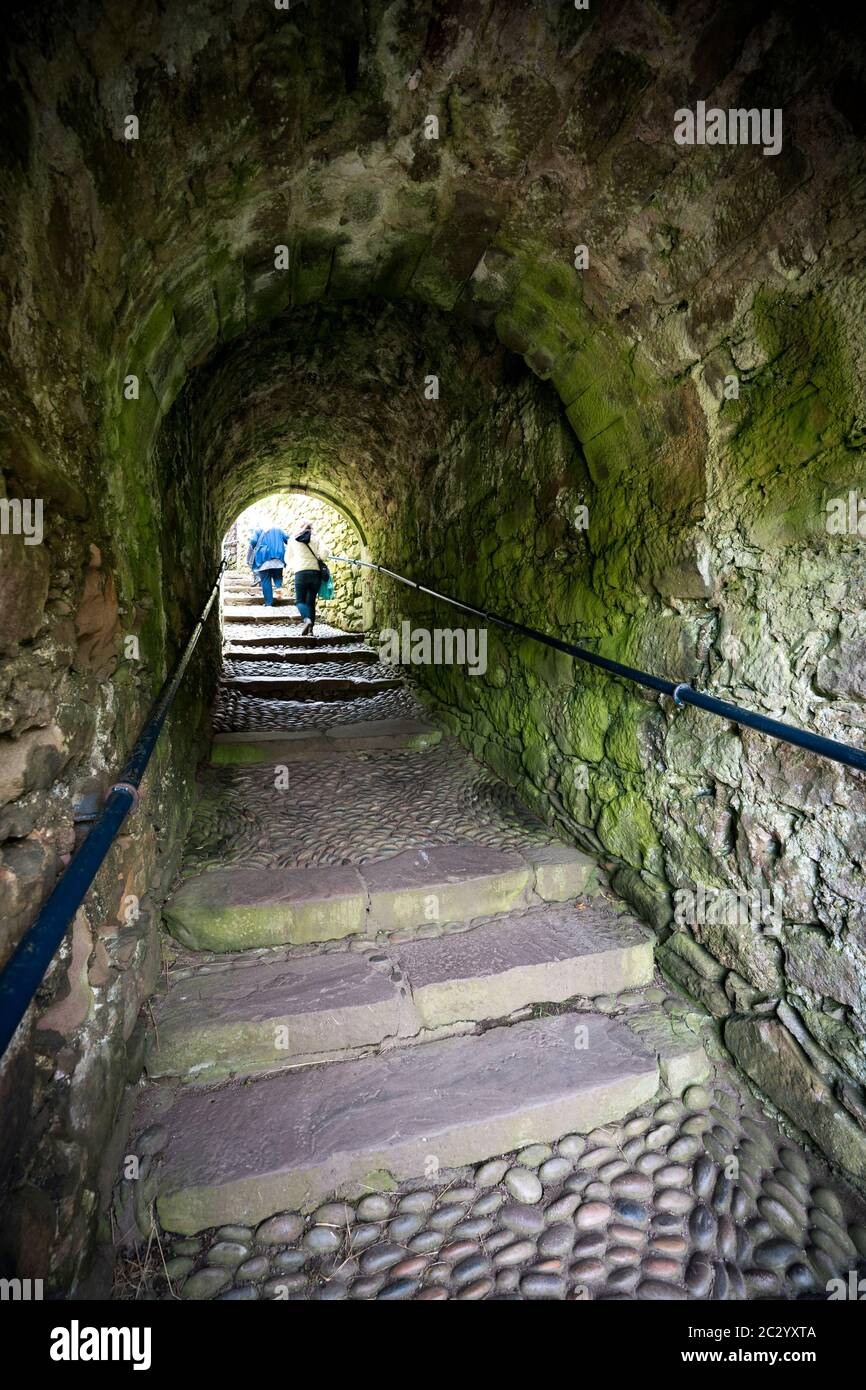 Dos personas suben las escaleras que conducen a través de un paso en arco de escalones de adoquines en el castillo de Dunnottar, Stonehaven, Escocia, Reino Unido, Europa Foto de stock