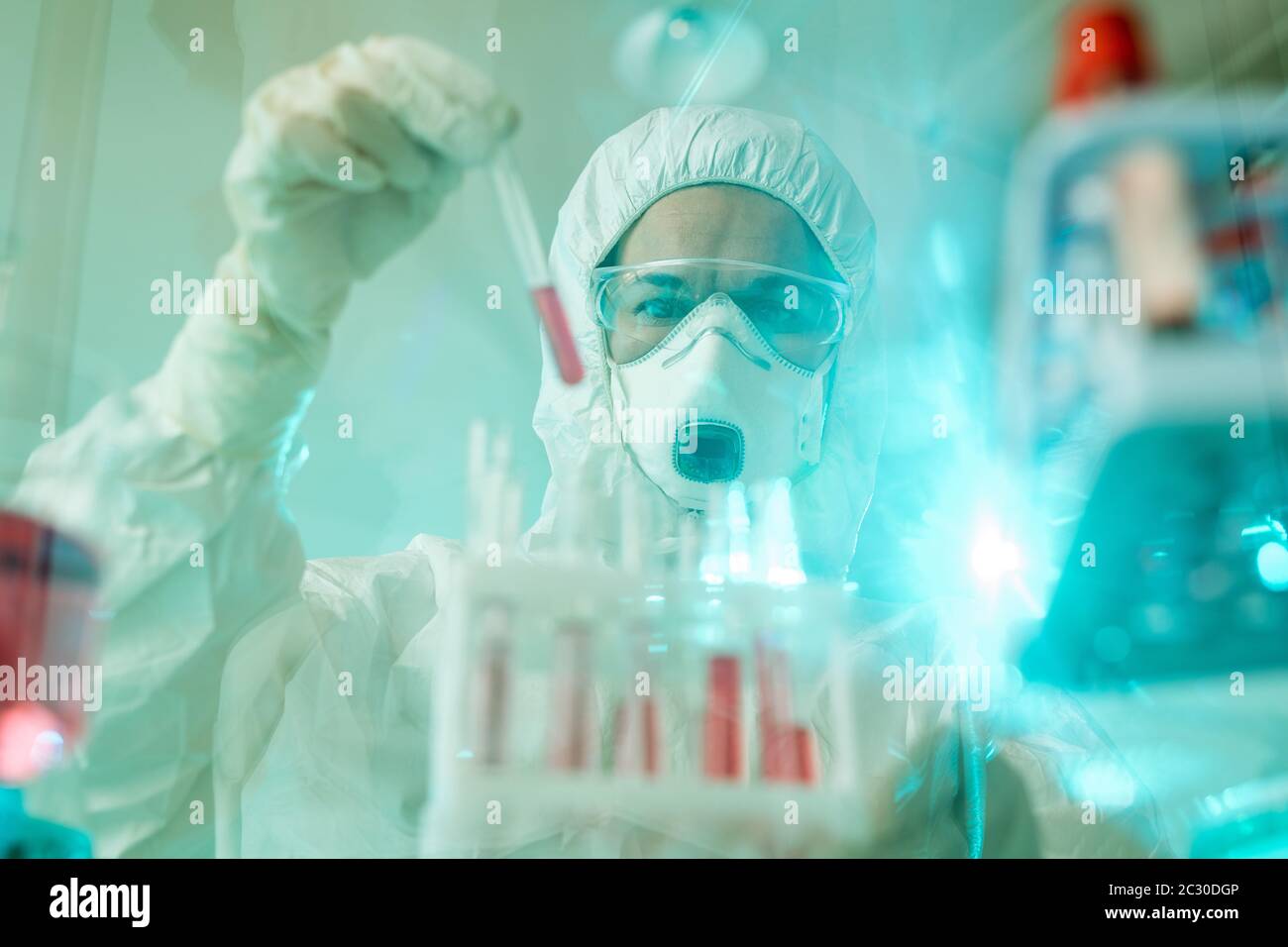 Especialista de laboratorio en traje protector y máscara que trabaja con muestras de sangre infectadas Foto de stock