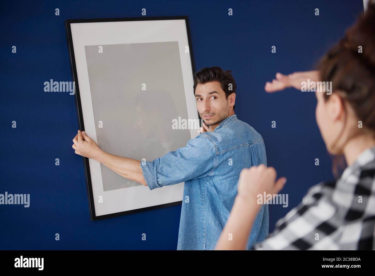 Pareja colgando un marco de fotos en la pared azul Foto de stock
