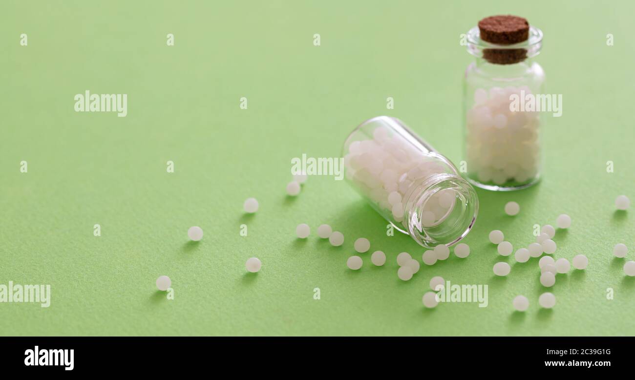 Homeopatía, glóbulos esparcidos por botella de vidrio, fondo verde. Medicina alternativa natural, espacio de copia Foto de stock