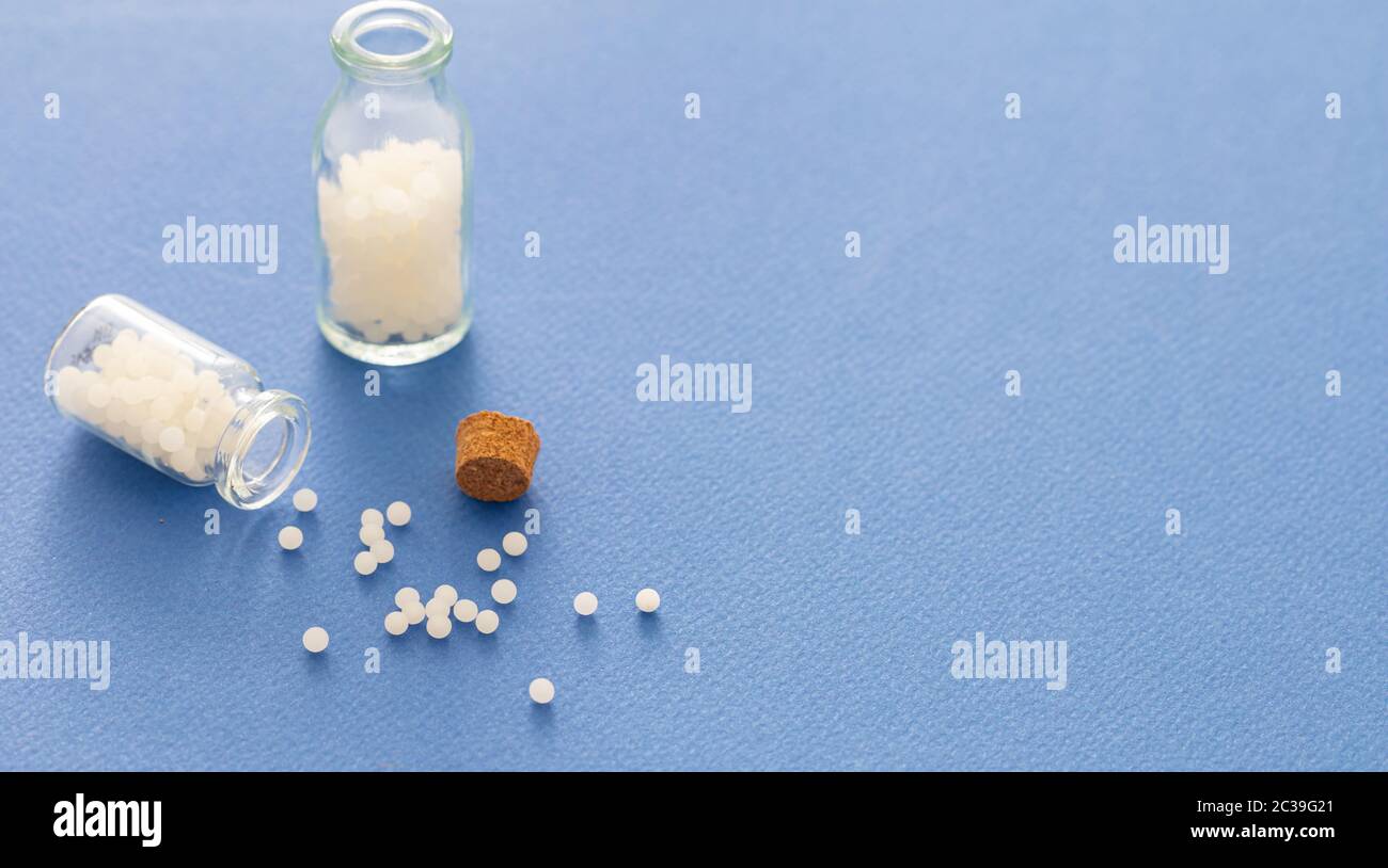 Homeopatía, glóbulos esparcidos por una botella de vidrio, fondo azul. Medicina alternativa natural, espacio de copia Foto de stock
