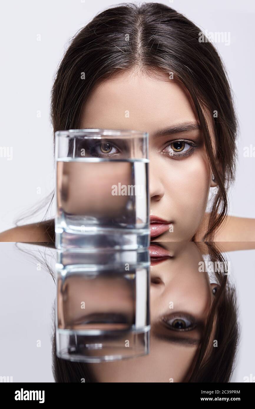 La chica esconde su cara detrás de un vaso con agua. Retrato de la belleza  de la joven en la mesa del espejo Fotografía de stock - Alamy