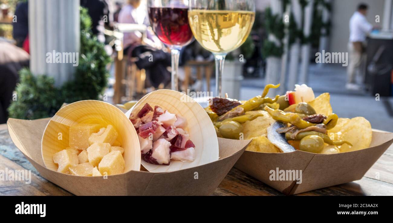 Panorama del bar de tapas. Queso, jamón y pinchos con vino tinto y blanco sobre una mesa de madera en una cafetería al aire libre Foto de stock