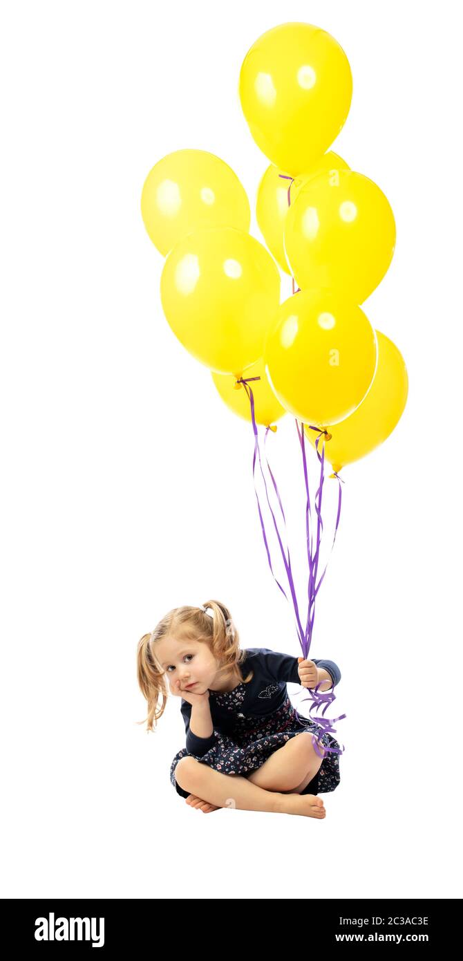 Aburrido niña sentada en el suelo sujetando globos de colores en la mano. Aislado en blanco. Foto de stock