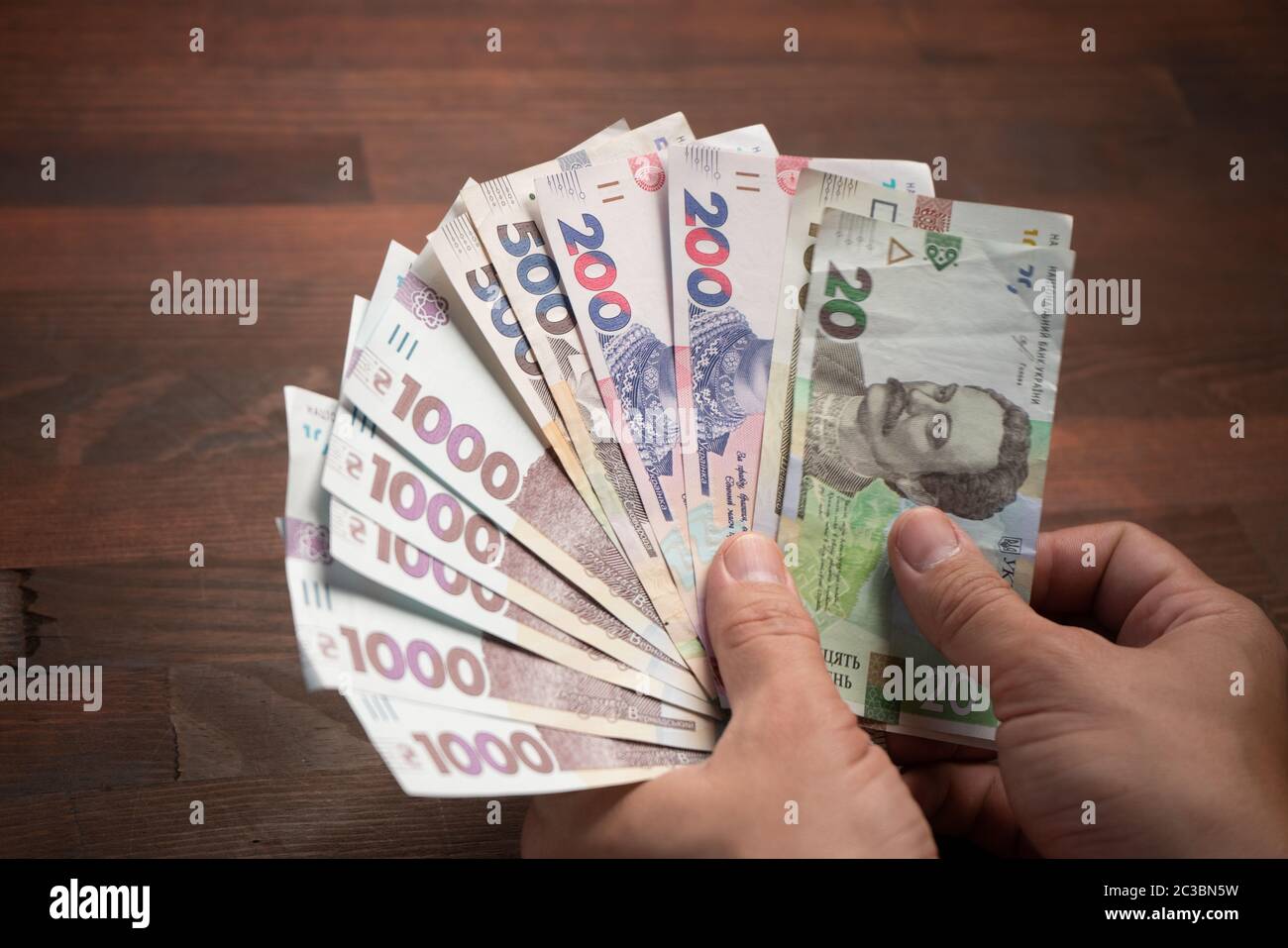 Manos macho con ventilador de billetes. El hombre caucásico tiene un paquete de nuevas hryvnias ucranianas contra el fondo de la mesa de madera. Primer plano. Dinero en efectivo Foto de stock