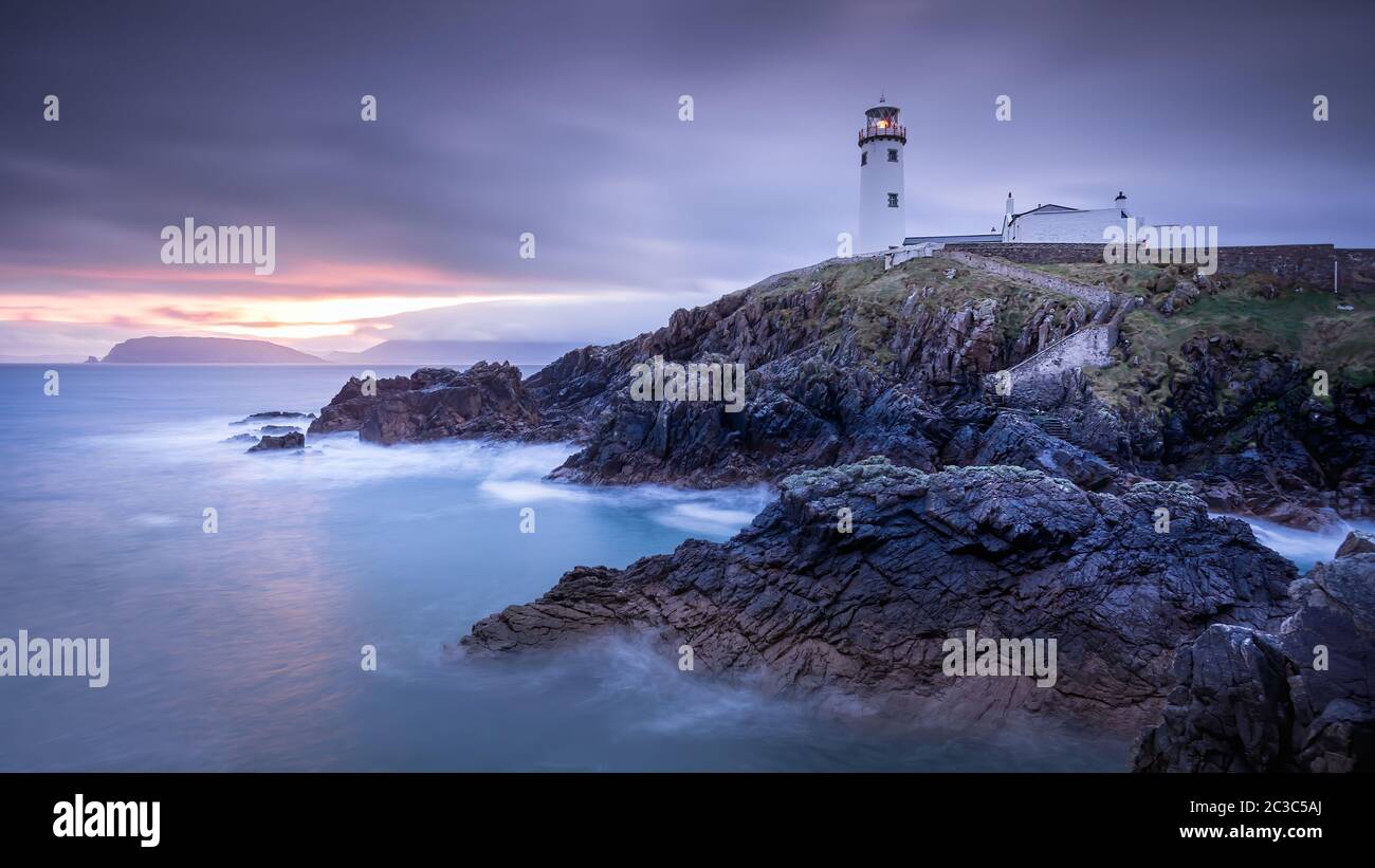 Crepúsculo se rinde al amanecer, amanecer en el faro de Fanad Head con aguas borrosas del Océano Atlántico Foto de stock