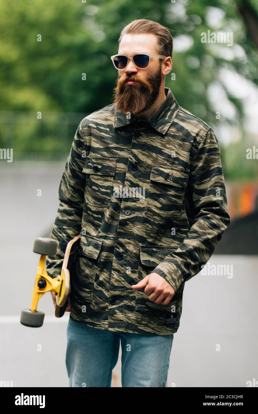 Hombre barbudo sosteniendo el longboard o el skateboard en el parque. Foto de stock