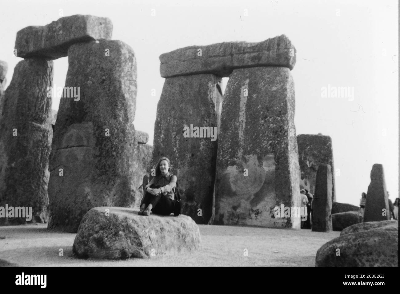 Muchacha sentada en una piedra en Stone Henge Inglaterra muchacha del Reino Unido en piedra en círculo druida famosa de la edad de piedra se sienta mujer sentada que presenta vieja prohibición de la bomba Foto de stock