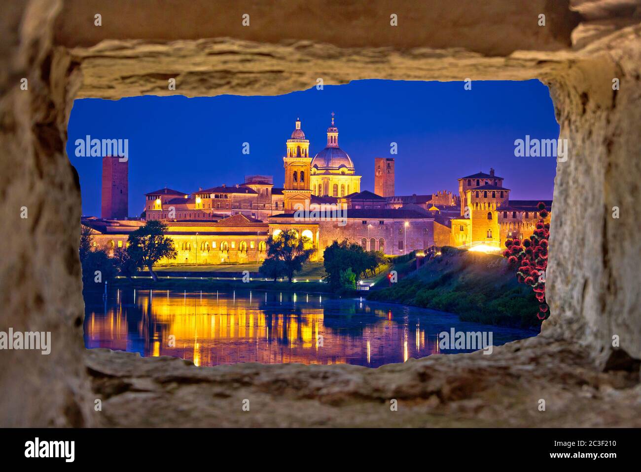 Vista nocturna del horizonte de la ciudad de Mantova a través de una ventana de piedra Foto de stock