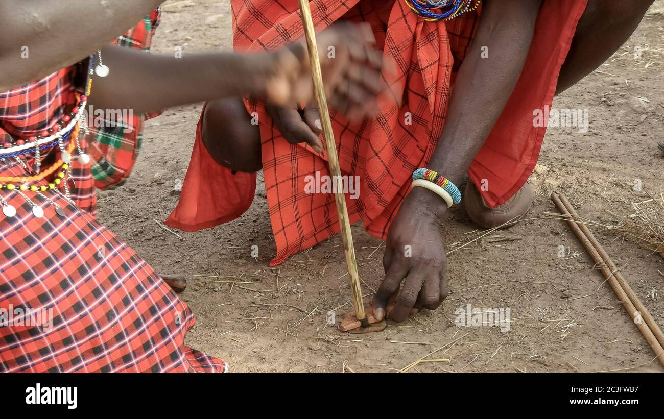 dos hombres masai usan un taladro de mano para iniciar un incendio en una manyatta en kenia Foto de stock
