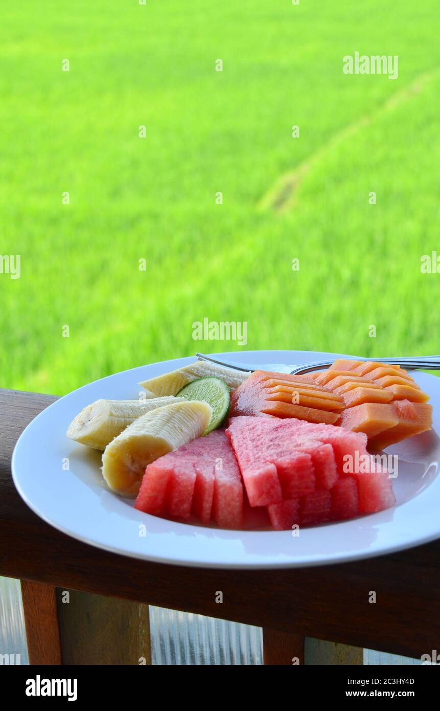 Plato de fruta tropical deliciosa y fresca con el fondo del campo de arroz. Sandía, plátano y papaya comen con jugo de lima. Foto de stock