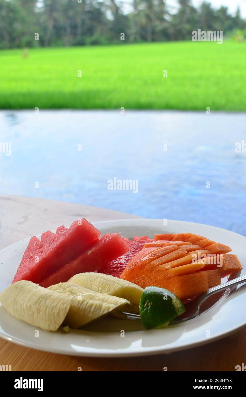 Plato de fruta tropical deliciosa y fresca con el fondo del campo de arroz. Sandía, plátano y papaya comen con jugo de lima. Foto de stock