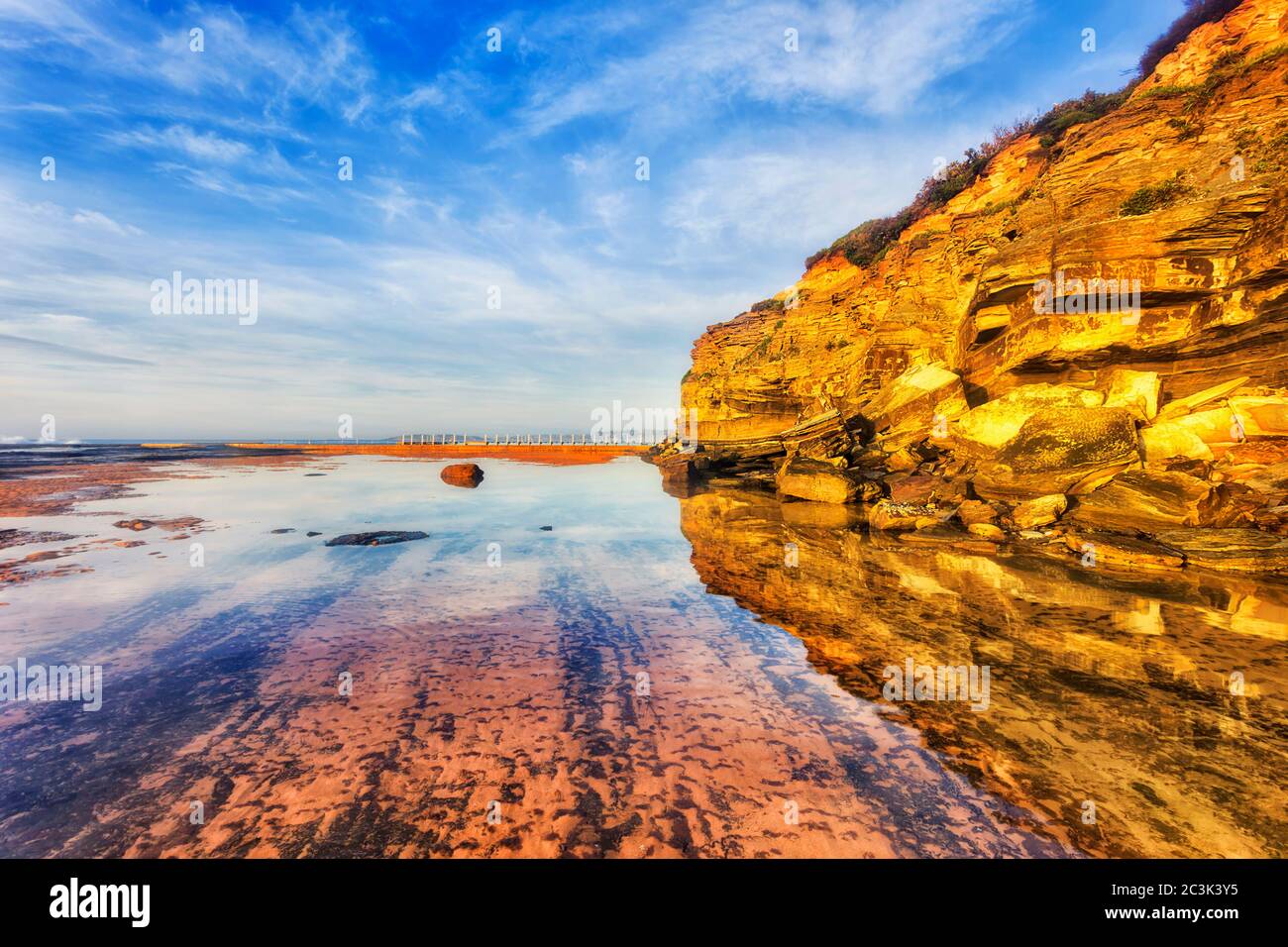 Rocas de arenisca de Narrabeen cabo sobre el fondo del mar de la playa de Narrabeen en la marea baja bajo el cálido sol del amanecer. Foto de stock