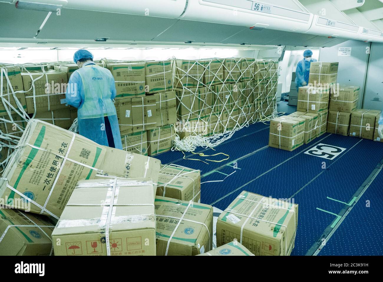 Cargadores chinos con trajes de hazmat cargando a un pasajero convertido en avión de carguero con máscaras quirúrgicas y batas para luchar contra el Pandemia de COVID Foto de stock