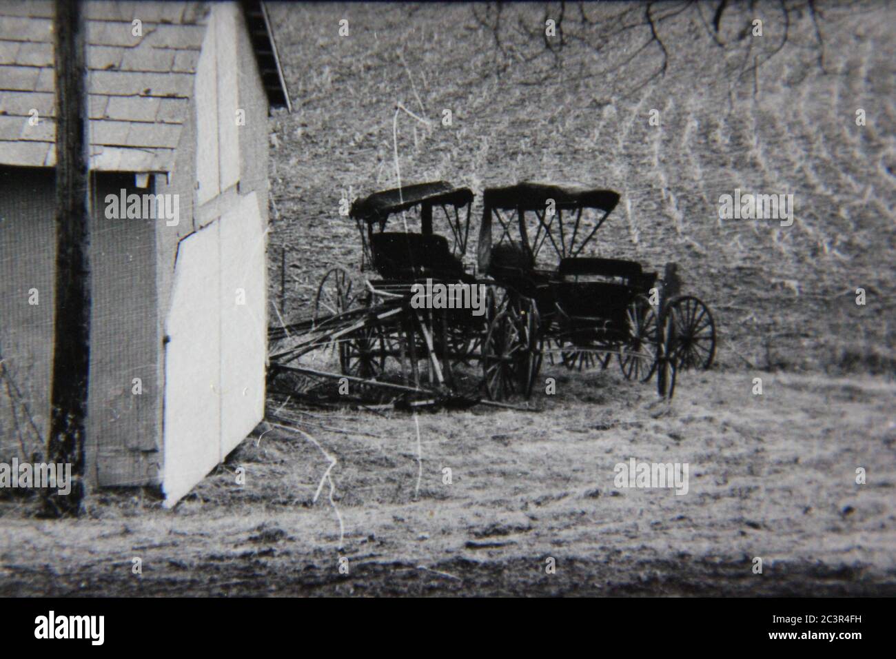 Fotografía en blanco y negro de la cosecha de los 70 de dos buggies Amish estacionados detrás del granero. Foto de stock