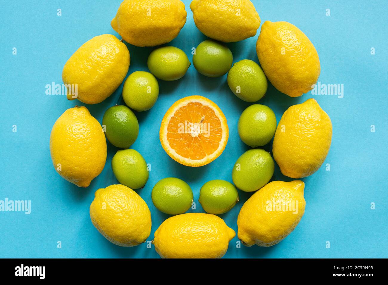 vista superior de limones amarillos maduros, naranja y limas dispuestas en círculos sobre fondo azul Foto de stock